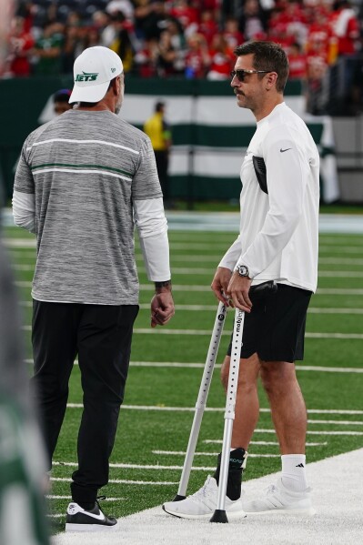 New York Jets quarterback Aaron Rodgers, right, stands on the field with crutches before an NFL football game between the New York Jets and the Kansas City Chiefs, Sunday, Oct. 1, 2023, in East Rutherford, N.J. (AP Photo/Frank Franklin II)