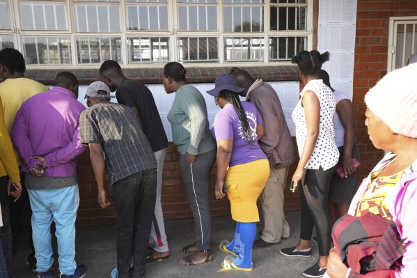 People look for their names, outside a polling station in Harare, Thursday, Aug. 24, 2023. Voting is still underway in Zimbabwe. Hours long delays in distributing ballot papers forced the president to extend the general election by a day at dozens of polling stations. (AP Photo/Tsvangirayi Mukwazhi)