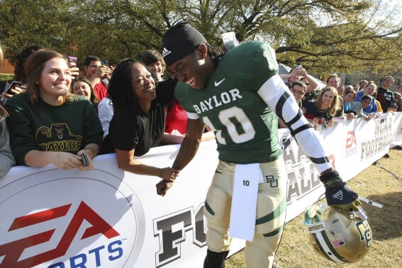 Heisman Trophy-winner and former Baylor quarterback Robert Griffin III is greeted by Holly Johnson on the Baylor campus, Monday, Feb. 27, 2012, in Waco, Texas, where he posed for photos for EA Sports NCAA Football 13 video game to be released in July. Video-game developer EA Sports is breaking back into the college football world 11 years after lawsuits over using players’ likeness without compensation froze the franchise. (Jerry Larson/Waco Tribune-Herald via AP)