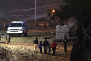 Migrants traveling with children walk up a hill to a waiting U.S. Border Patrol agent just inside San Ysidro, Calif., after climbing over the border wall from Playas de Tijuana, Mexico, Monday, Dec. 3, 2018. Thousands of Central American migrants who traveled with recent caravans want to seek asylum in the United States but face a decision between crossing illegally or waiting months, because the U.S. government only processes a limited number of those cases a day at the San Ysidro border crossing. (AP Photo/Rebecca Blackwell)