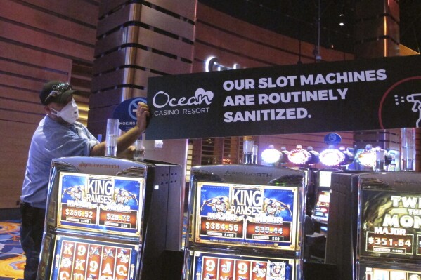 A worker at the Ocean Casino Resort in Atlantic City N.J. installs a sign indicating that slot machines will routinely be sanitized once the casino reopened a month later to prevent the spread of the coronavirus, June 3, 2020. The New Jersey Supreme Court is expected to hear arguments, Wednesday, Sept. 27, 2023, in a case involving whether insurance companies were correct in denying payouts to the casino for business losses during the state-mandated closure in 2020. (AP Photo/Wayne Parry)