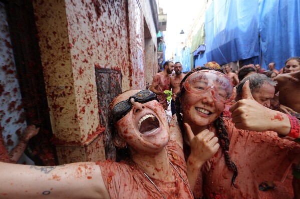 Women react as they throw tomatoes at each other during the annual "Tomatina", tomato fight fiesta, in the village of Bunol near Valencia, Spain, Wednesday, Aug. 30, 2023. Thousands gather in this eastern Spanish town for the annual street tomato battle that leaves the streets and participants drenched in red pulp from 120,000 kilos of tomatoes. (AP Photo/Alberto Saiz)