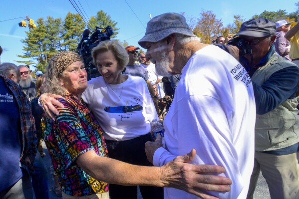 Mimi Wright, Margaret Carpenter, and Irv Puskin embrace in a hug after the unveiling of a new roadside marker that recognized Burton Snowboards, Tuesday, Oct. 3, 2023, along Main Street in Londonderry, Vt. (Kristopher Radder/The Brattleboro Reformer via AP)