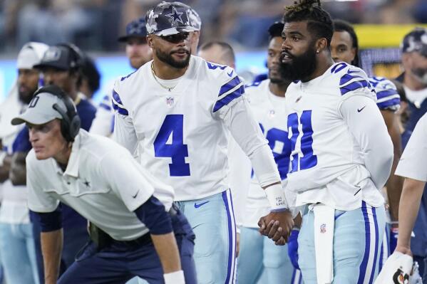 Dallas Cowboys quarterback Dak Prescott (4) holds hands with running back Ezekiel Elliott (21) during the second half of a preseason NFL football game against the Los Angeles Chargers Saturday, Aug. 20, 2022, in Inglewood, Calif. (AP Photo/Ashley Landis)