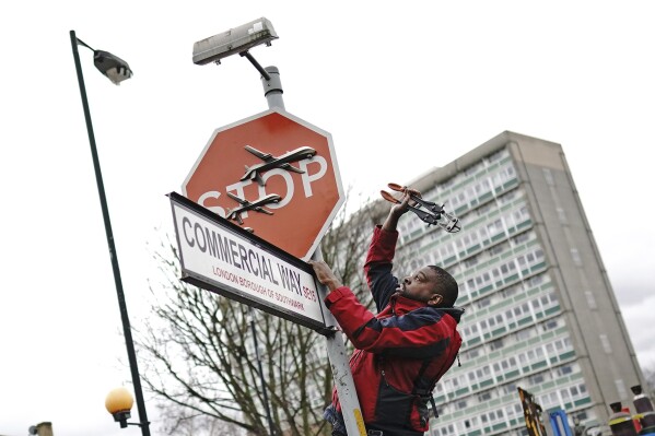 A person removes a piece of art work by Banksy, which shows what looks like three drones on a traffic stop sign, which was unveiled at the intersection of Southampton Way and Commercial Way in Peckham, south east London, Friday Dec. 22, 2023. (Aaron Chown/PA via AP)