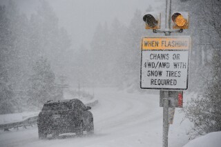 FILE - A car passes a caution sign as heavy snow falls on the Mt. Rose Highway near Reno, Nev., on Dec. 1, 2022. The National Weather Service issued advisories Saturday, Nov. 18, 2023, along the California-Nevada line ahead of an early winter storm that could bring more than a foot (30 centimeters) of snow to the upper elevations of the Sierra and winds gusting up to 100 mph (160 kph) over ridgetops. The winter weather advisories, in effect from 4 p.m. Saturday through 4 a.m. Sunday, stretched from the Lake Tahoe area near Reno to south of Yosemite National Park, including Mammoth Lakes, California. (Jason Bean/The Reno Gazette-Journal via AP, File)