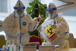 FILE - Health workers wearing protective suits put COVID-19 test samples into a bag at a hotel used for people to stay during a period of health quarantine on March 20, 2022, in the Yanqing district of Beijing. China on Friday, Sept. 30, 2022 dismissed complaints from two U.S. congressmembers over the quarantining of American diplomats and their family members under the country's strict COVID-19 regulations. (AP Photo/Andy Wong, File)