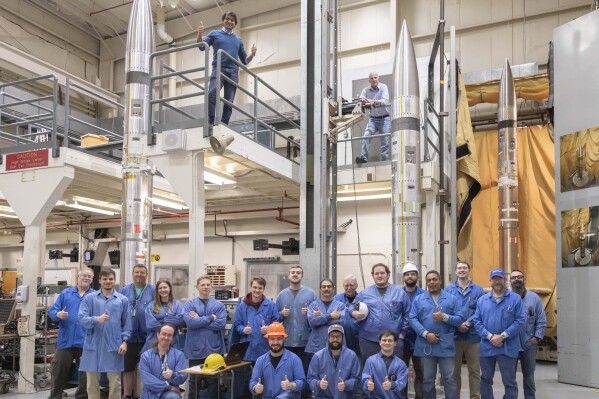 This photo provided by NASA shows three APEP rockets at NASA Wallops Flight Facility on Wallops Island, Va., on Feb. 21, 2024, with Mission Principal Investigator Dr. Barjatya, top left, and NASA Mission Manager Jay Scott, top right, and Embry-Riddle Aeronautical University and NASA personnel. During the April 8, 2024 total solar eclipse, the rockets will blast off with science instruments into the electrically charged portion of the atmosphere near the edge of space known as the ionosphere. (Berit Bland/NASA via AP)