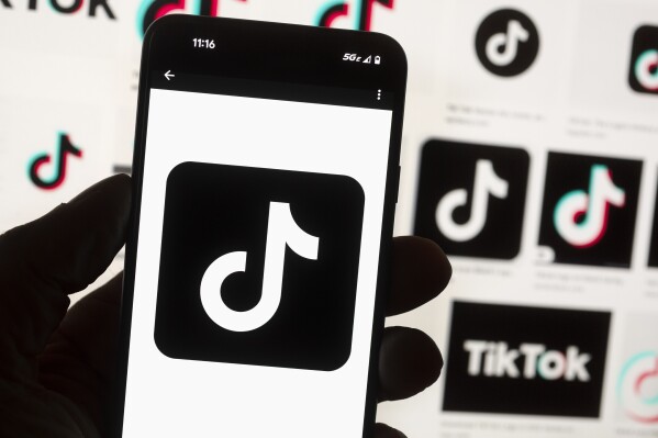 FILE - The TikTok logo is displayed on a mobile phone in front of a computer screen, Oct. 14, 2022, in Boston. TikTok will begin labeling content created using artificial intelligence when it's uploaded from certain platforms. TikTok says its efforts are an attempt to combat misinformation from being spread on its social media platform. The announcement came on ABC's “Good Morning America” on Thursday, May 9, 2024. (Ǻ Photo/Michael Dwyer, File)