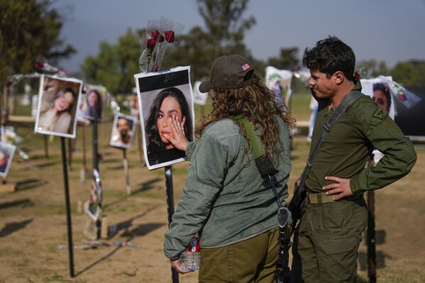 Israeli soldiers look at photos of people killed and taken captive by Hamas militants during their violent rampage through the Nova music festival in southern Israel, which are displayed at the site of the event, to commemorate the October 7, massacre, near kibbutz Re'im, Friday, Dec. 1, 2023. (AP Photo/Ariel Schalit)