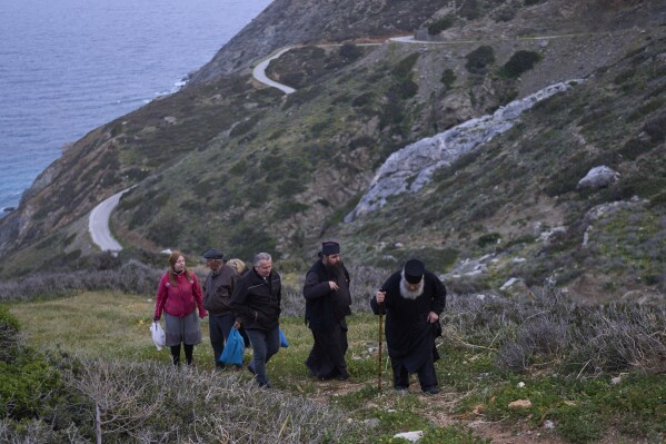 O monge cristão ortodoxo Padre Spyridon de Amorgos, à direita, o Padre Antonis e outros fiéis deixam a capela de Panagia Evangelistria, após participarem da Divina Liturgia na ilha de Amorgos, Grécia, na segunda-feira, 24 de março de 2025. (Foto AP/Petros Giannakouris)