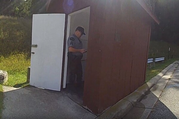 In this photo released by the Michigan State Police, a Department of Natural Resources sergeant stands in the doorway of an outhouse after a woman became trapped in the toilet after attempting to retrieve her Apple Watch, Tuesday, Sept. 19, 2023, at Dixon Lake in Bagley Township, Mich. (Michigan State Police via AP)
