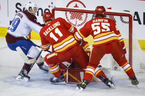 Colorado Avalanche forward Nathan MacKinnon watches as the puck crosses the line as Calgary Flames forward Mikael Backlund, center, and defenseman Noah Hanifin watch during the first period of an NHL hockey game Thursday, Oct. 13, 2022, in Calgary, Alberta. (Jeff McIntosh/The Canadian Press via AP)