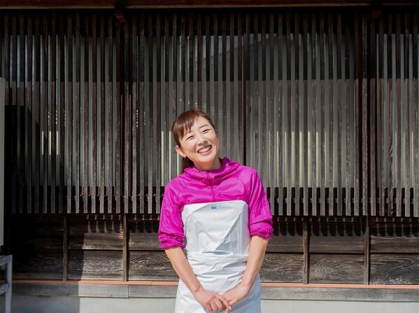 In this undated photo provided by Yoshie Minamidani, Minamidani poses in front of her seafood store in Wajima, Ishikawa prefecture, Japan. Minamidani is a survivor of a powerful earthquake that hit western Japan on New Year’s Day. The seafood store she ran in Wajima, the hardest hit city, was seriously damaged, as was the storage filled with her precious preserved fish. She told The Associated Press Tuesday she is determined to bring Wajima back. (Yoshie Minamidani via AP)