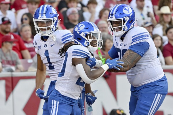 BYU running back Deion Smith, center, celebrates with teammates Keanu Hill, left, and Kingsley Suamataia, right, after scoring a touchdown against Arkansas during the first half of an NCAA college football game, Saturday, Sept. 16, 2023, in Fayetteville, Ark. (AP Photo/Michael Woods)