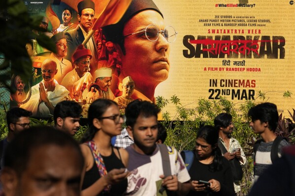 People walk past a large poster of the movie Swatantra Veer Savarkar displayed outside a cinema hall in Mumbai, India, Thursday, Mar. 21, 2024. The movie, set to be released on Friday, is one of several upcoming Bollywood releases based on polarizing issues, which either promote Indian Prime Minister Narendra Modi and his government’s political agenda, or lambast his critics. (AP Photo/Rajanish Kakade)