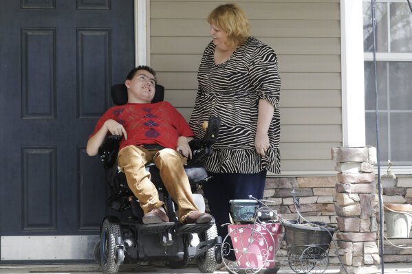 In this April 14, 2020, photo, Jodi Hansen talks with her son Jacob Hansen at their home, in Eagle Mountain, Utah. Even before the new coronavirus hit, cystic fibrosis meant a cold could put Jacob Hansen in the hospital for weeks. He relies on hand sanitizer and disinfecting wipes to keep germs at bay because has cerebral palsy and uses a wheelchair, but these days shelves are often bare. For millions of disabled people and their families, the coronavirus crisis has piled on new difficulties and ramped up those that already existed. (AP Photo/Rick Bowmer)