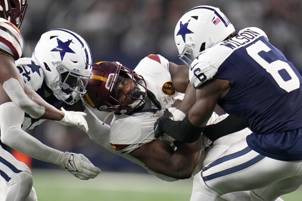 Washington Commanders running back Brian Robinson Jr., middle, is tackled between Dallas Cowboys cornerback DaRon Bland, left, and safety Donovan Wilson (6) during the second half of an NFL football game Thursday, Nov. 23, 2023, in Arlington, Texas. (AP Photo/Julio Cortez)