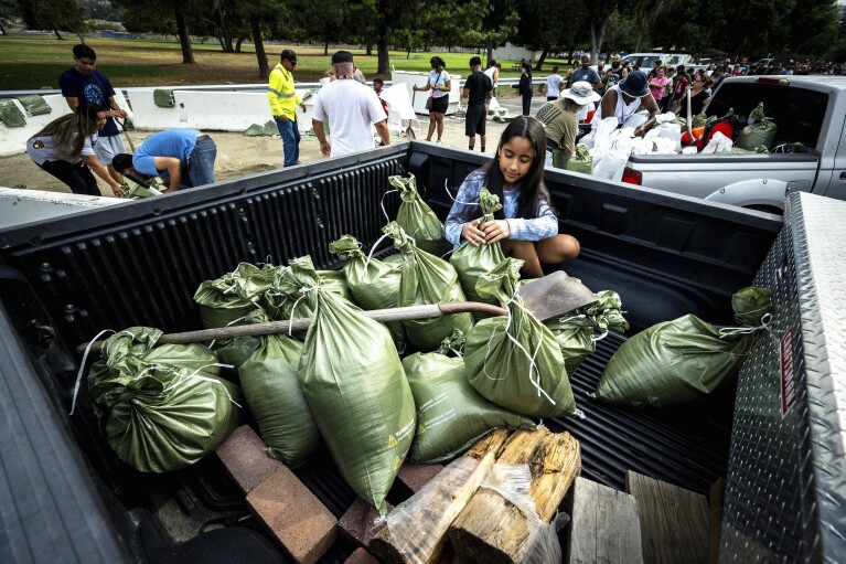 Madeline Noble, de 9 años, sentada en la parte trasera de la camioneta de su padre mientras ayuda con sacos de arena en Wildwood Park en San Bernardino, California, el sábado 19 de agosto de 2023, mientras los residentes se preparan para la llegada del huracán Hilary.  (Watchara Phomicinda/The Orange County Register vía AP)