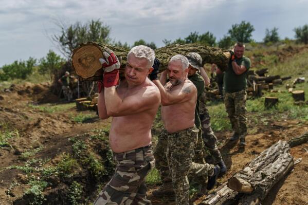 Members of the Dnipro-1 regiment carry logs to fortify their position near Sloviansk, Donetsk region, eastern Ukraine, Friday, Aug. 5, 2022. While the lull in rocket strikes has offered a reprieve to remaining residents, some members of the Ukrainian unit say it could be a prelude to renewed Russian attacks. (AP Photo/David Goldman)