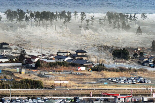 FILE - Waves from a tsunami hit residences after a powerful earthquake in Natori, Miyagi prefecture, Japan, on March 11, 2011. Japan on Monday, March 11, 2024, marked 13 years since a massive earthquake and tsunami hit the country’s northern coasts. (Kyodo News via AP, File)