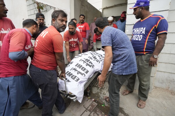 Men carry a body in Karachi, Pakistan, Saturday, Nov. 25, 2023. At least 10 people were killed and 22 injured in the blaze at RJ Mall on Rashid Minhas Road in Karachi. (AP Photo/Fareed Khan)