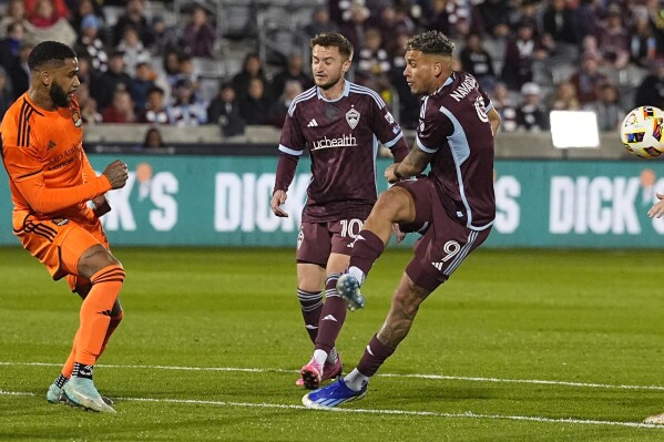 The ball whistles past Colorado Rapids forward Rafael Navarro (9) after his kick was blocked by Houston Dynamo defender Micael in the first half of an MLS soccer match Saturday, March 23, 2024, in Commerce City, Colo. (AP Photo/David Zalubowski)