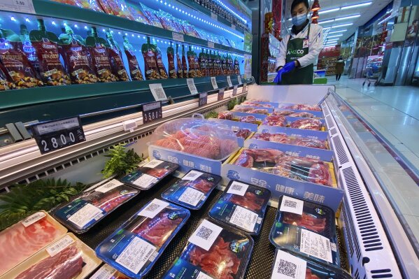 A worker wearing a mask and gloves stand near beef products from New Zealand packaged with a QR-code linked to its coronavirus test results displayed at a supermarket in Beijing, Tuesday, Nov. 24, 2020. China has stirred controversy with claims it has detected the coronavirus on packages of imported frozen food. (AP Photo/Ng Han Guan)