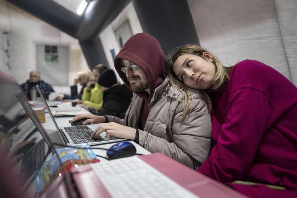 A couple uses a laptop at the heating tent "Point of Invincibly" in Bucha, Ukraine, Monday, Nov. 28, 2022. (AP Photo/Evgeniy Maloletka)