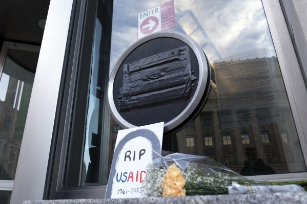 Flowers and a sign are placed outside the headquarters of the U.S. Agency for International Development, or USAID, Feb. 7, 2025, in Washington. (AP Photo/Jose Luis Magana, file)