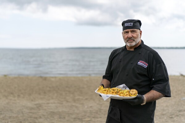 Executive chef John Bordieri is photographed with a dish of calamari outside Iggy's Boardwalk restaurant Friday, June 7, 2024, in Warwick, R.I. This year, the "calamari comeback" chef might not be coming back. Bordieri became known as the "calamari ninja" for standing wordlessly, clad head-to-toe in black, and holding a platter of sauteed squid during a video roll call of states that nominated Joe Biden during the 2020 Democratic National Convention. But he now says he hasn't heard from state or national leaders about a repeat performance at this summer's party's convention in Chicago. (AP Photo/David Goldman)