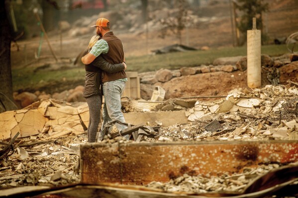 FILE - Chris and Nancy Brown embrace while searching through the remains of their home, leveled by the Camp Fire, in Paradise, Calif., on Nov. 12, 2018. The Camp Fire bears many similarities to the deadly wildfire in Hawaii. Both fires moved so quickly residents had little time to escape. (AP Photo/Noah Berger, File)