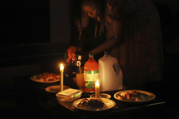A woman prepares a meal by candle light at her home in Harare, Zimbabwe, Tuesday, Dec. 20, 2022. A buoyant holiday mood is not lifting the country which is coping with widespread power outages and the world's highest food inflation. (AP Photo)