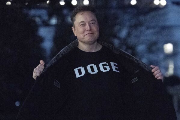 Elon Musk flashes his T-shirt that reads "DOGE" to the media as he walks on South Lawn of the White House, in Washington, March 9, 2025. (AP Photo/Jose Luis Magana, File)