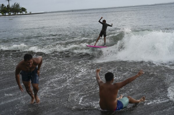 Kids surf small waves along the beach after school in Teahupo'o, Tahiti, French Polynesia, Monday, Jan. 15, 2024. (AP Photo/Daniel Cole)