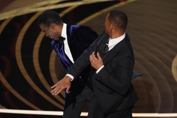 FILE - Will Smith, right, hits presenter Chris Rock on stage while presenting the award for best documentary feature at the Oscars on Sunday, March 27, 2022, at the Dolby Theatre in Los Angeles. Rock was the first artist to perform on Netflix's first-ever live, global streaming event. (AP Photo/Chris Pizzello, File)