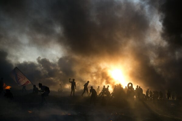 
              Black smoke from burning tires covers the sky over Palestinian protesters hurl stones toward Israeli troops during a protest at the Gaza Strip's border with Israel, Friday, Oct. 12, 2018. (AP Photo/Khalil Hamra)
            