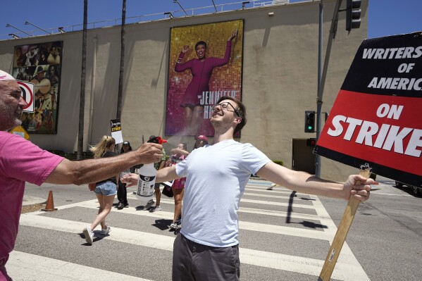 Luke DePalatis, right, gets a cooling spritz of water from Michael Abel during a rally by striking writers and actors outside Warner Bros. studios Friday, July 14, 2023, in Burbank, Calif. Both are with the WGA. This marks the first day actors formally joined the picket lines, more than two months after screenwriters began striking in their bid to get better pay and working conditions and have clear guidelines around the use of AI in film and television productions. (AP Photo/Mark J. Terrill)