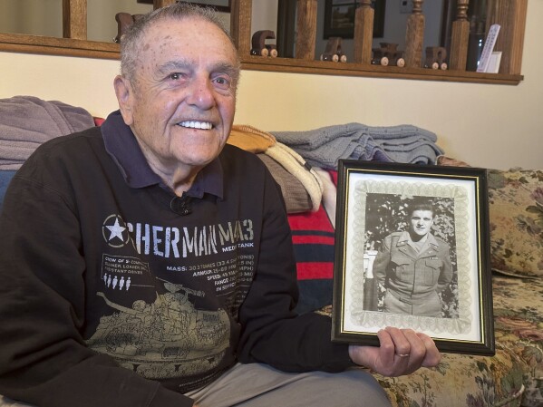 World War II veteran Andy Negra sits in his home in Helen, Ga, on April 10, 2024. He shows a photo of himself during his time with the Army's 128th Armored Field Artillery Battalion, 6th Armored Division. (AP Photo/Sharon Johnson)