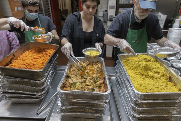 Nicholas Loud, left, Sophie Thurschwell, center, and Peter Woll prepare lunch boxes at Community Help in Park Slope, a soup kitchen and food pantry better known as CHiPS, on Friday, June 16, 2023 in New York. Charitable giving in the United States declined in 2022. The downturn in giving has led to issues at CHiPS, as it has in many charities across the country. (AP Photo/Jeenah Moon)