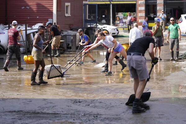 Volunteers clean up a downtown parking area on the banks of the Winooski River, Wednesday, July 12, 2023, in Montpelier, Vt. Following a storm that dumped nearly two months of rain in two days, Vermonters are cleaning up from the deluge of water. (AP Photo/Charles Krupa)