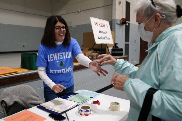 Diane Roy, election warden of Ward 5, hands out a sticker to a voter at the Gov. James B. Longley Campus, Tuesday, Nov. 7, 2023, in Lewiston, Maine. The city is working to return to normalcy following the mass shooting that killed 18 less than two weeks ago. (AP Photo/Robert F. Bukaty)