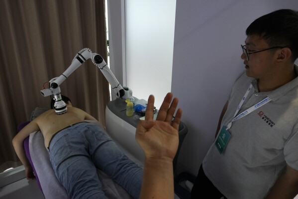 An exhibitor watches a visitor receiving a massage by a robotic arm during the annual World Robot Conference at the Etrong International Exhibition and Convention Center on the outskirts of Beijing, Thursday, Aug. 17, 2023. (AP Photo/Andy Wong)