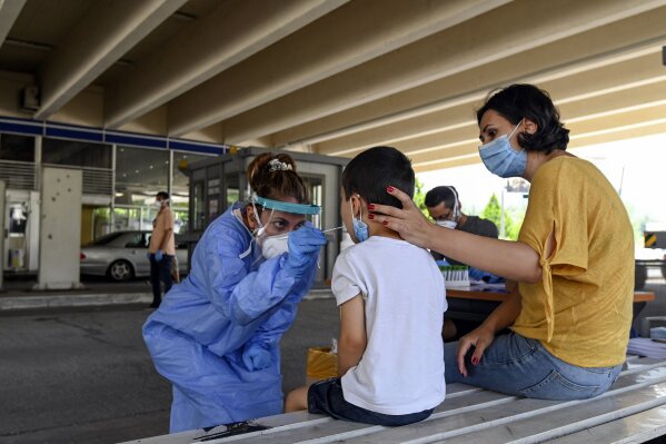 A health worker wearing protective gear takes swab samples from tourists to test for the coronavirus, at Promahonas border crossing with Bulgaria, which is the only land border into Greece that is open on Monday, July 6, 2020. Dozens of vehicles of Serb holidaymakers who were trapped at the Greek border overnight have been allowed to cross into Greece after a ban on the entry of people from Serbia came into effect due to a coronavirus flare-up in Serbia. (AP Photo/Giannis Papanikos)