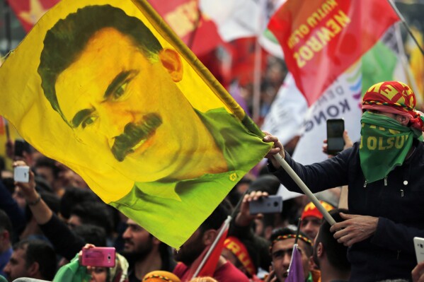 In this file photo dated Wednesday, March 21, 2018, a youth holds a flag with the image of Abdullah Ocalan, the jailed leader of the rebel Kurdistan Workers' Party, or PKK, in Istanbul, Turkey. (AP Photo/Lefteris Pitarakis, File)