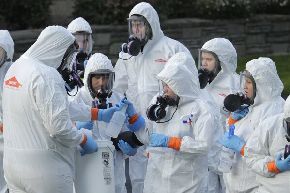 Workers from a Servpro disaster recovery team wearing protective suits and respirators are given supplies as they line up before entering the Life Care Center in Kirkland, Wash., to begin cleaning and disinfecting the facility, Wednesday, March 11, 2020. The nursing home is at the center of the coronavirus outbreak in Washington state. For most people, the virus causes only mild or moderate symptoms. For some it can cause more severe illness, especially in older adults and people with existing health problems. (AP Photo/Ted S. Warren)