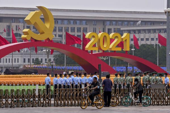 People cycle past Chinese paramilitary police standing in formation near seating and a platform with a Communist Party's logo setup on Tiananmen Square in Beijing, Monday, June 28, 2021. China is marking the centenary of its ruling Communist Party this week by heralding what it says is its growing influence abroad, along with success in battling corruption at home. (AP Photo/Andy Wong)