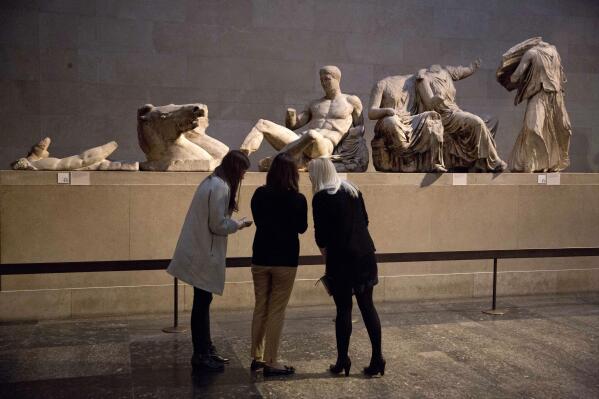 FILE - Women stand by a marble statue of a naked youth thought to represent Greek god Dionysos, center, from the east pediment of the Parthenon, on display during a media photo opportunity to promote a forthcoming exhibition on the human body in ancient Greek art at the British Museum in London, Thursday, Jan. 8, 2015. Greece is renewing a bid to seek the return of ancient sculptures removed from the Parthenon at the Acropolis in Athens more than 200 years ago from the British Museum, a government official said Monday, Nov. 15, 2021. (AP Photo/Matt Dunham, File)