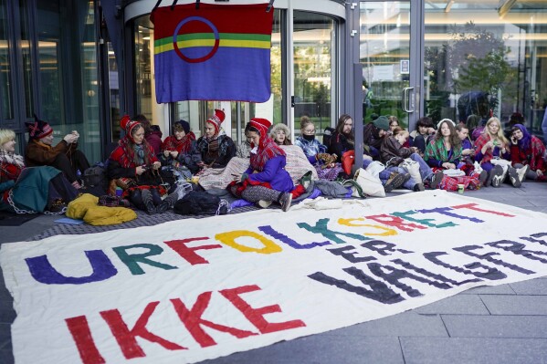 Activists wearing traditional Sami outfits sit in protest outside the entrance of Statkraft, a state-owned company that operates 80 of the wind turbines at Fosen, in central Norway’s Fosen district, about 450 kilometers (280 miles) north of the capital of Oslo, in Oslo, Thursday, Oct. 12, 2023. Dozens of activists in Norway on Thursday blocked the entrance to one of the main operators of a wind farm they say hinders the rights of the Sami Indigenous people to raise reindeer. Writing on banner reads 