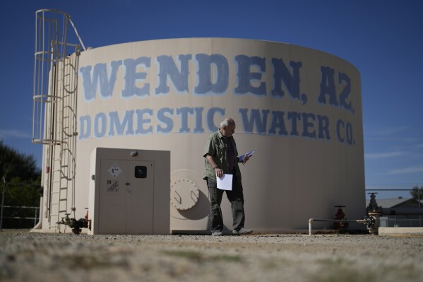 Gary Saiter, chairman of the board and general manager of the Wenden Domestic Water Improvement District, walks by a water tank at the district's well Tuesday, Oct. 17, 2023, in Wenden, Ariz. According to Saiter, records indicate the water table at the utility's well have dropped several hundred feet since the 1940s. He believes the state needs to implement controls to help preserve the aquifer. (AP Photo/John Locher)